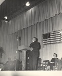 Guest Speaker at Podium, Faye Patterson Bonds Seated on Stage by unknown