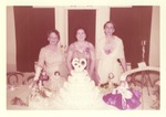 Three Women Dressed in Formals Stand Behind Cake Topped with “60” and Surrounded by Dolls by unknown